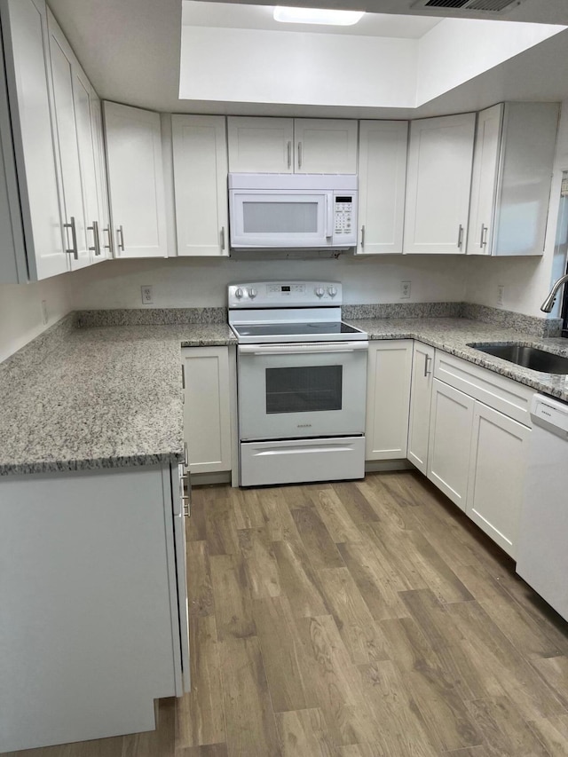 kitchen with light stone countertops, white appliances, sink, hardwood / wood-style flooring, and white cabinetry