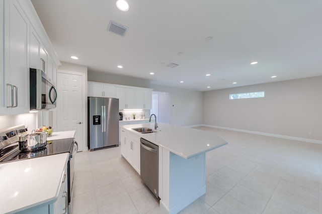 kitchen featuring light tile patterned flooring, sink, appliances with stainless steel finishes, a kitchen island with sink, and white cabinets