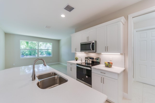 kitchen with backsplash, appliances with stainless steel finishes, light tile patterned floors, sink, and white cabinets