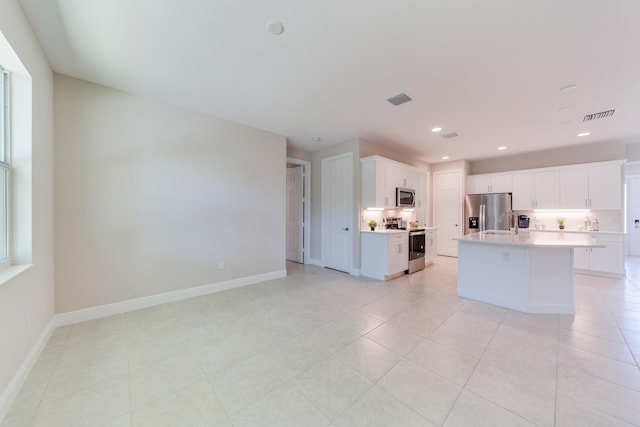 kitchen featuring stainless steel appliances, white cabinets, sink, tasteful backsplash, and an island with sink