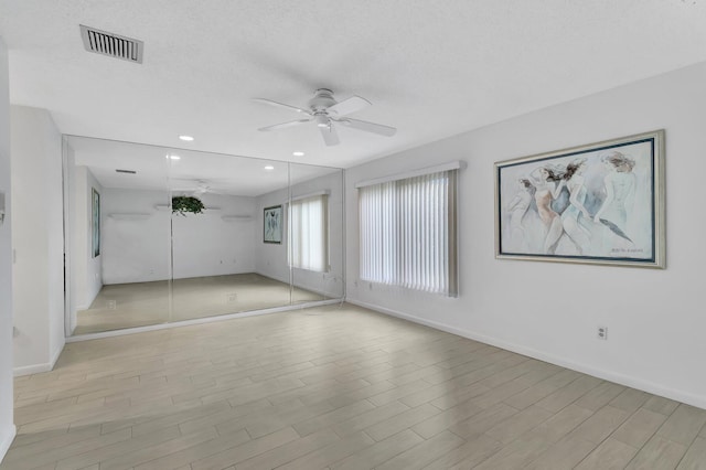 spare room featuring a textured ceiling, light wood-type flooring, and ceiling fan