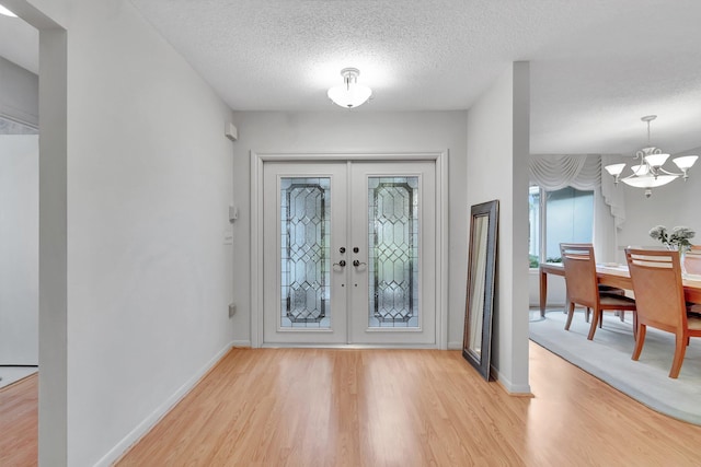 entryway featuring light hardwood / wood-style floors, an inviting chandelier, a textured ceiling, and french doors