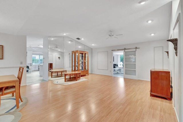 living room with ceiling fan, a barn door, light hardwood / wood-style floors, and vaulted ceiling