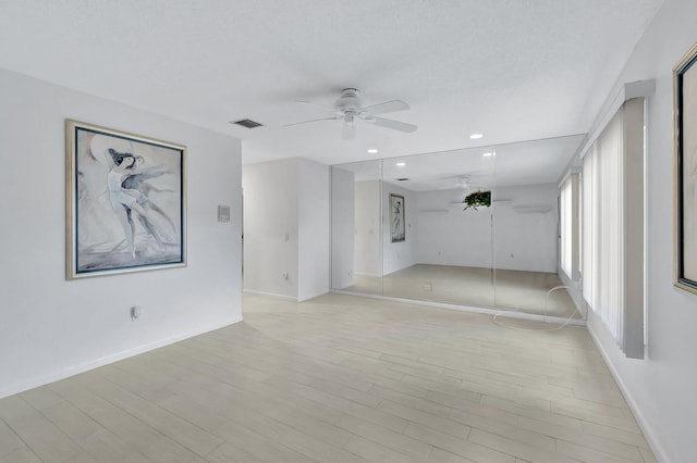 empty room with ceiling fan, a textured ceiling, and light wood-type flooring