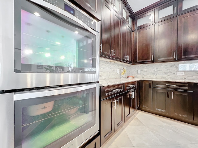 kitchen with dark brown cabinets, decorative backsplash, light stone counters, and stainless steel double oven