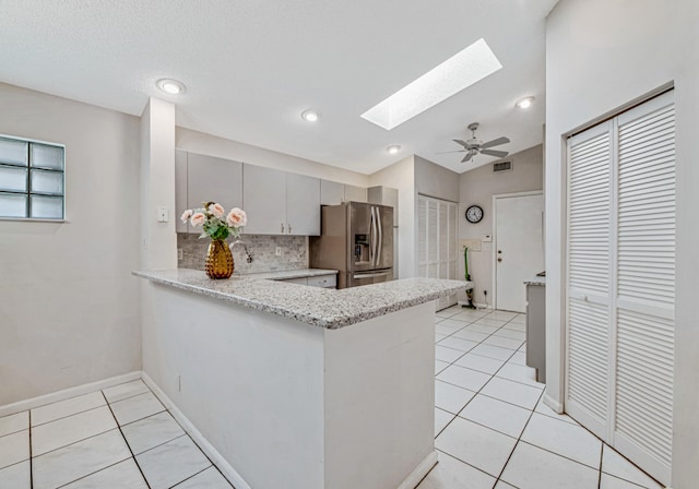 kitchen featuring a skylight, ceiling fan, kitchen peninsula, stainless steel fridge, and decorative backsplash