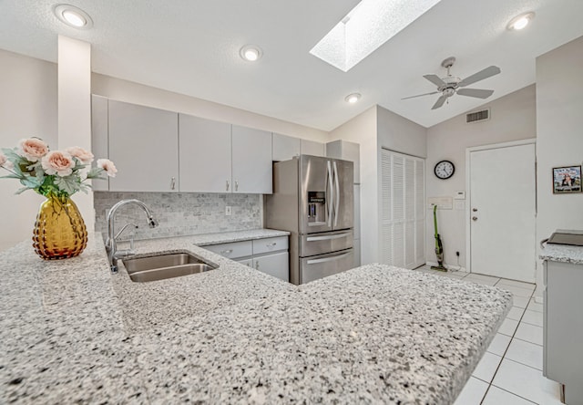 kitchen featuring kitchen peninsula, stainless steel fridge, gray cabinetry, vaulted ceiling with skylight, and sink