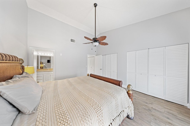 bedroom with light wood-type flooring, ensuite bath, two closets, ceiling fan, and high vaulted ceiling