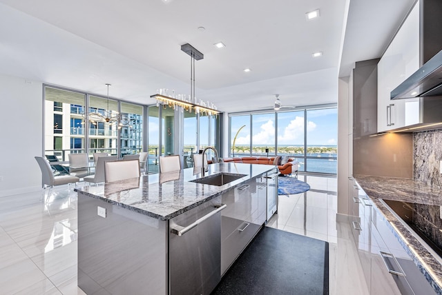 kitchen with a spacious island, wall chimney exhaust hood, modern cabinets, decorative light fixtures, and a sink