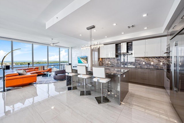 kitchen with white cabinetry, hanging light fixtures, wall chimney range hood, backsplash, and modern cabinets