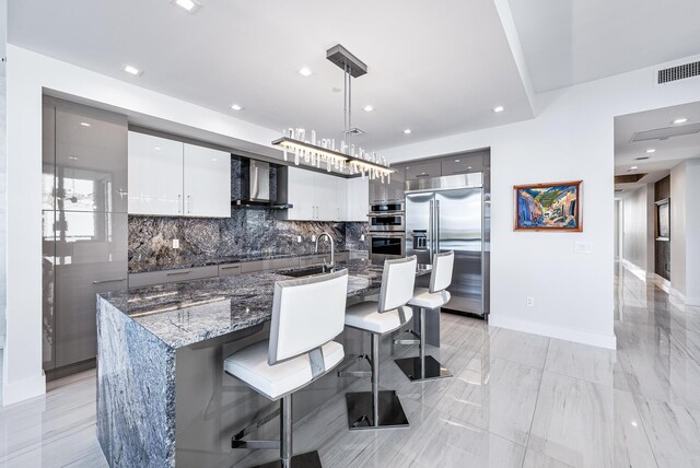 kitchen with white cabinetry, hanging light fixtures, wall chimney range hood, a kitchen breakfast bar, and backsplash