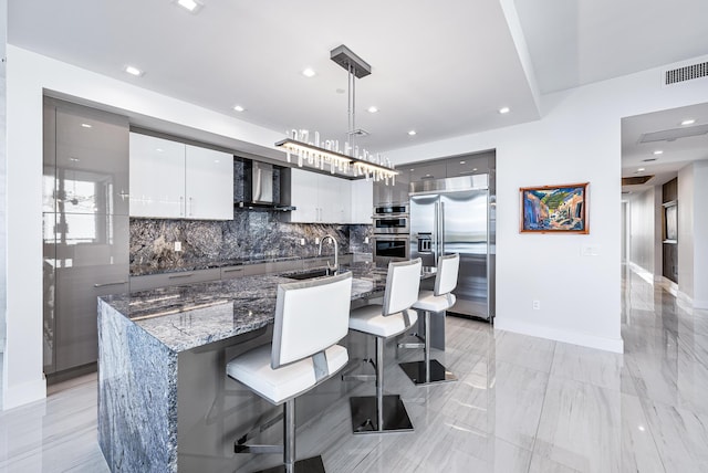 kitchen with backsplash, a kitchen breakfast bar, wall chimney range hood, appliances with stainless steel finishes, and decorative light fixtures