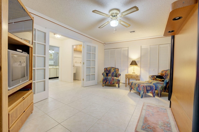 living area with washer / clothes dryer, a textured ceiling, ceiling fan, and light tile patterned floors