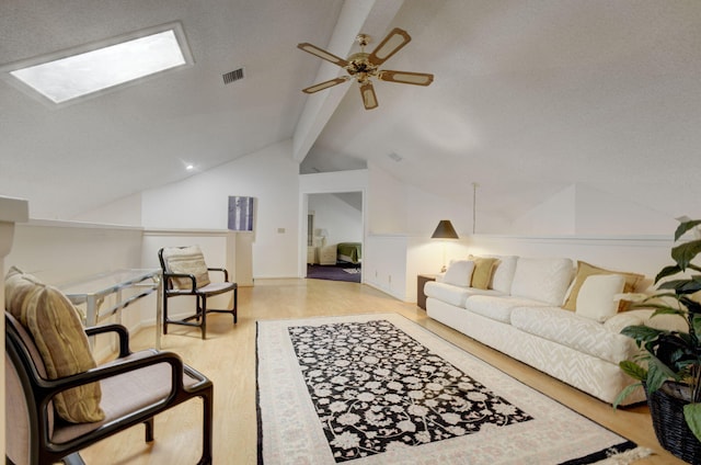 living room featuring vaulted ceiling with skylight, ceiling fan, and light wood-type flooring