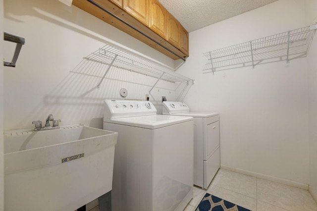 clothes washing area with cabinets, washing machine and dryer, a textured ceiling, and sink