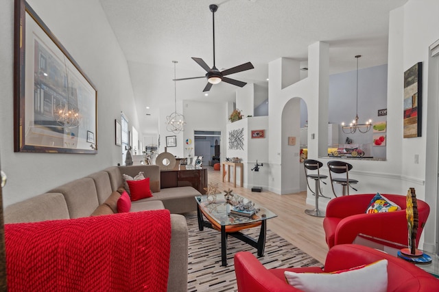 living room featuring ceiling fan with notable chandelier, high vaulted ceiling, a textured ceiling, and light wood-type flooring