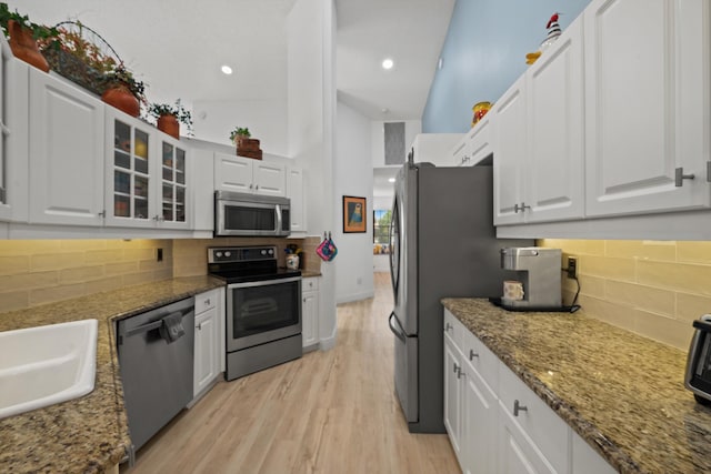 kitchen featuring stainless steel appliances, high vaulted ceiling, light hardwood / wood-style flooring, stone counters, and white cabinets