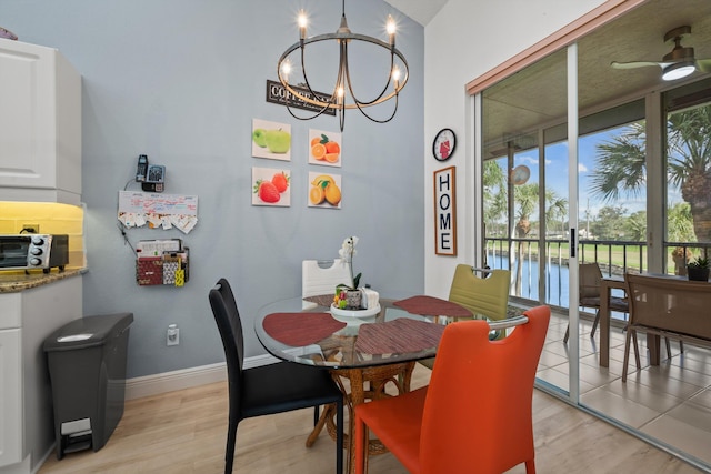 dining area with ceiling fan with notable chandelier, a water view, and light hardwood / wood-style floors