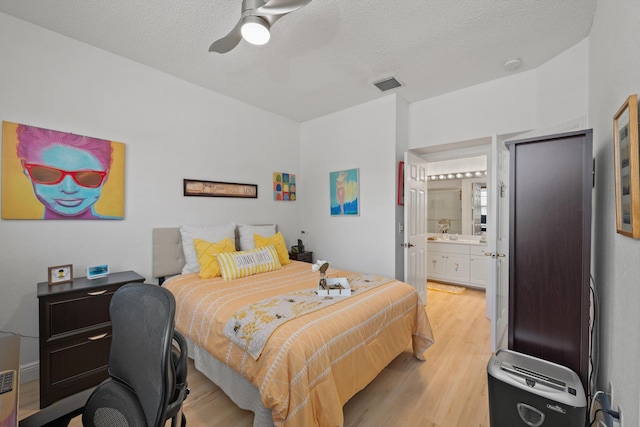 bedroom with a textured ceiling, ensuite bath, light hardwood / wood-style flooring, and ceiling fan