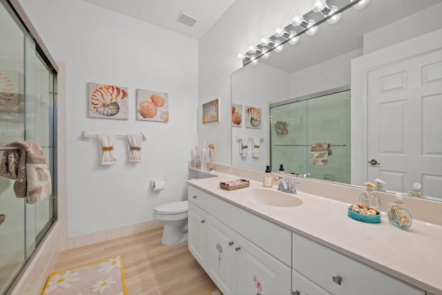 full bathroom with shower / bath combination with glass door, hardwood / wood-style floors, vanity, and toilet