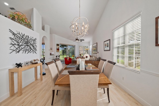 dining room featuring high vaulted ceiling, ceiling fan with notable chandelier, and light wood-type flooring