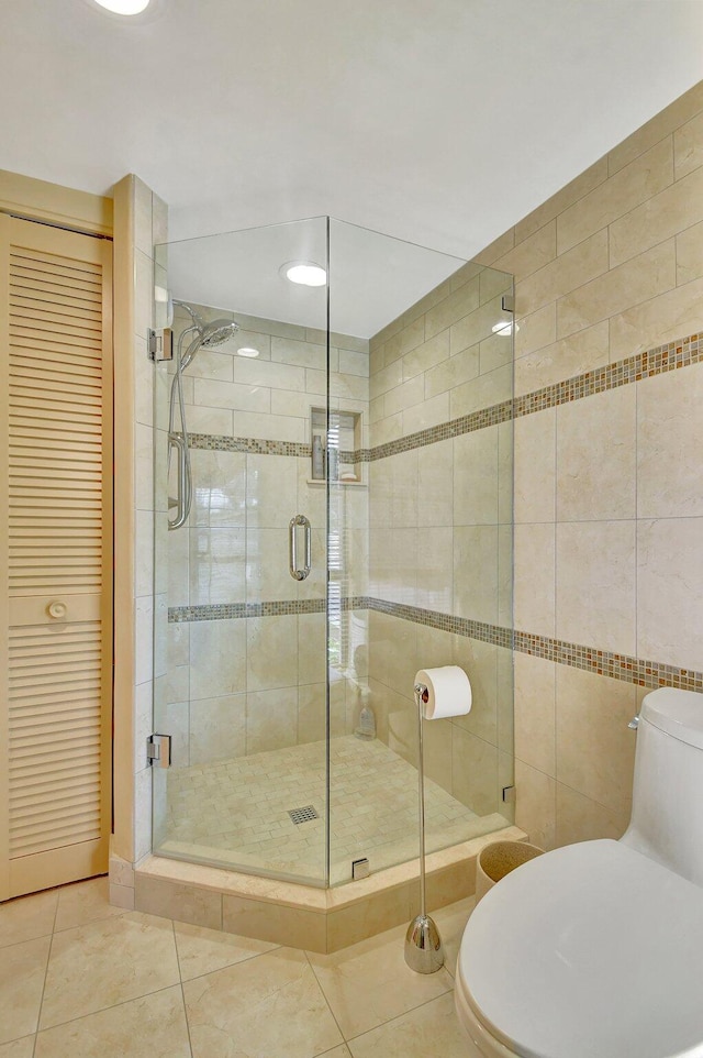 bathroom with walk in shower, toilet, tile patterned floors, and tile walls