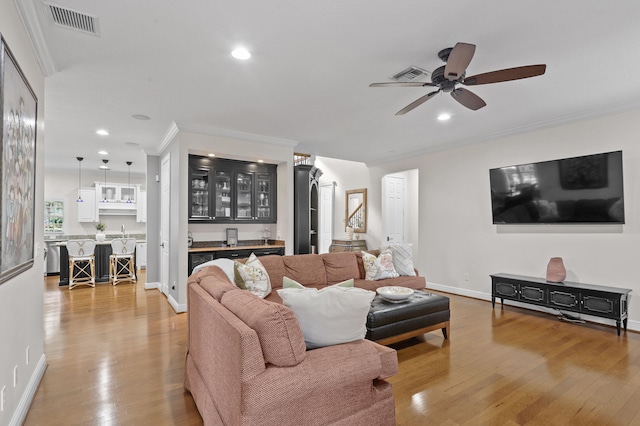 living room with ceiling fan, light hardwood / wood-style flooring, indoor bar, and ornamental molding