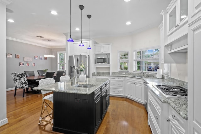 kitchen with crown molding, stainless steel appliances, decorative light fixtures, an island with sink, and light hardwood / wood-style flooring