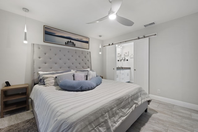 bedroom with a barn door, ensuite bath, and ceiling fan