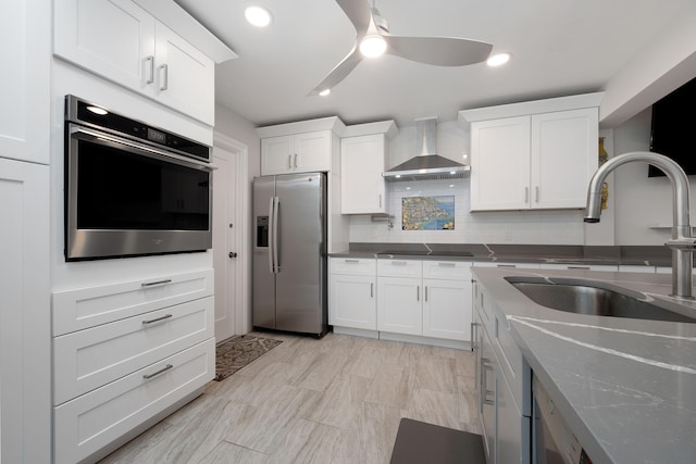 kitchen with wall chimney exhaust hood, ceiling fan, decorative backsplash, appliances with stainless steel finishes, and white cabinetry