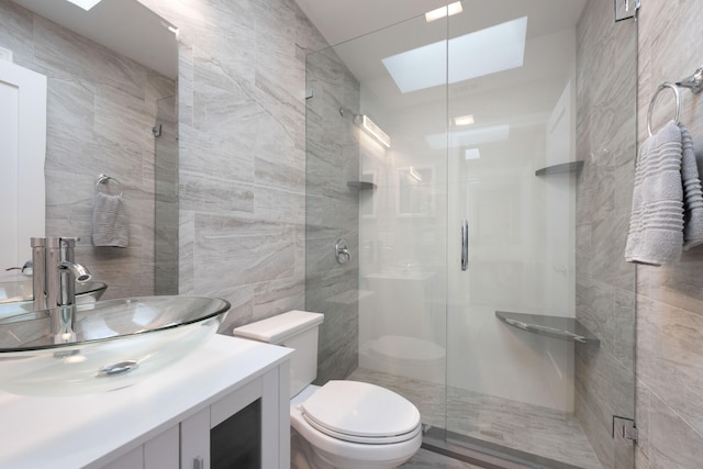 bathroom featuring a skylight, walk in shower, toilet, vanity, and tile walls