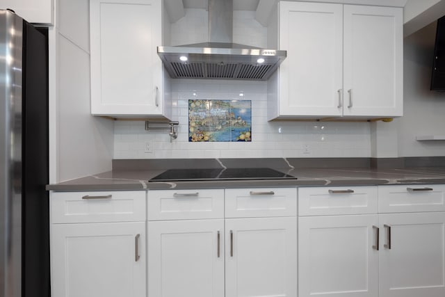 kitchen featuring decorative backsplash, stainless steel fridge, black electric stovetop, wall chimney range hood, and white cabinets