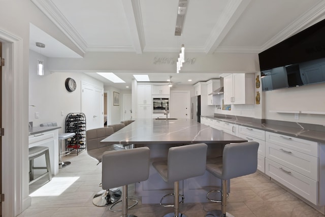 kitchen featuring a large island, beamed ceiling, stainless steel fridge, pendant lighting, and white cabinets