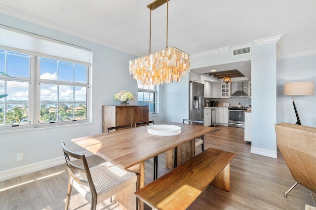 dining space featuring ornamental molding, light hardwood / wood-style floors, a healthy amount of sunlight, and an inviting chandelier