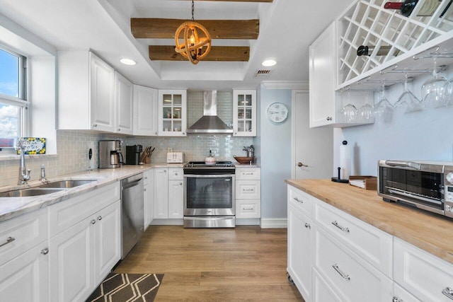 kitchen featuring wall chimney range hood, appliances with stainless steel finishes, sink, white cabinets, and light hardwood / wood-style flooring