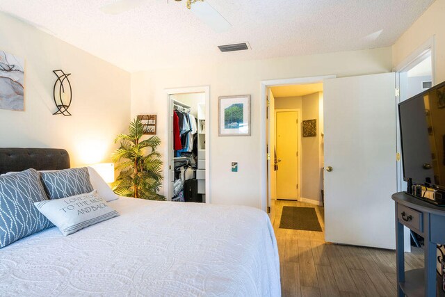 bedroom with wood-type flooring, a textured ceiling, ceiling fan, a closet, and a walk in closet