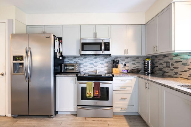 kitchen with stainless steel appliances, light stone countertops, light hardwood / wood-style floors, and decorative backsplash