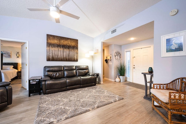 living room with ceiling fan, lofted ceiling, a textured ceiling, and light hardwood / wood-style floors