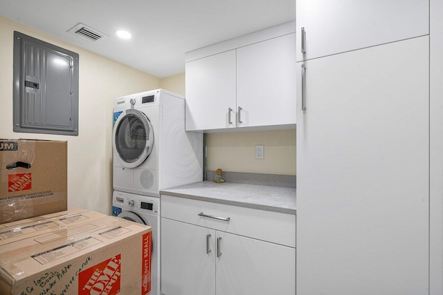 washroom featuring electric panel, cabinets, and stacked washer and dryer