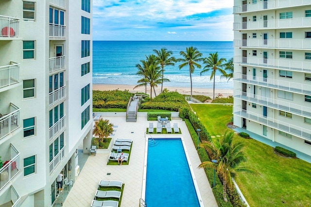 view of swimming pool with a lawn, a beach view, a water view, and a patio area