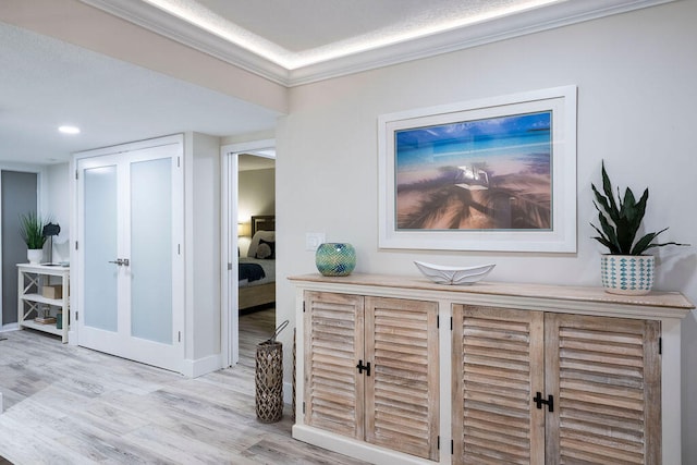 hall with light wood-type flooring, a textured ceiling, and ornamental molding