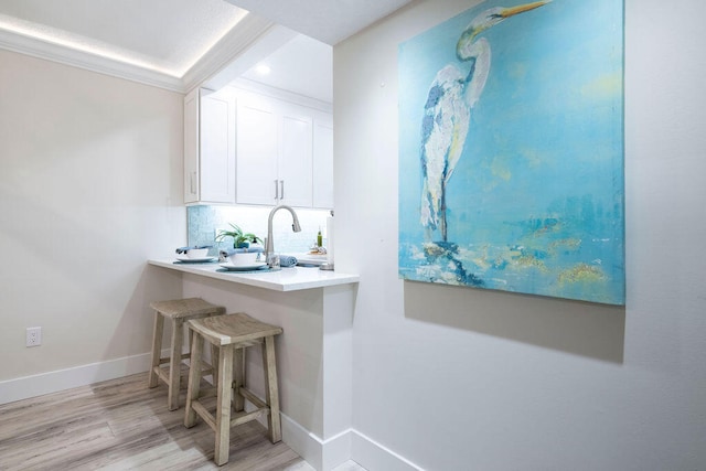 bar featuring tasteful backsplash, crown molding, light wood-type flooring, white cabinetry, and sink