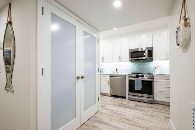 kitchen with light hardwood / wood-style flooring, appliances with stainless steel finishes, decorative backsplash, and white cabinets