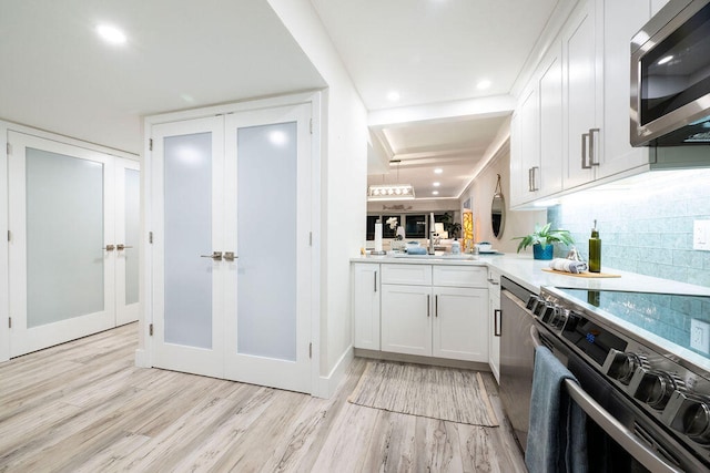 kitchen with light hardwood / wood-style floors, decorative backsplash, appliances with stainless steel finishes, white cabinets, and french doors