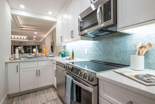 kitchen featuring stainless steel appliances, sink, backsplash, white cabinetry, and light wood-type flooring