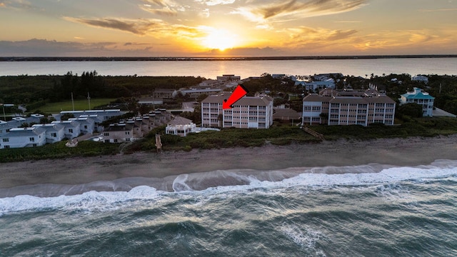 aerial view at dusk featuring a view of the beach and a water view