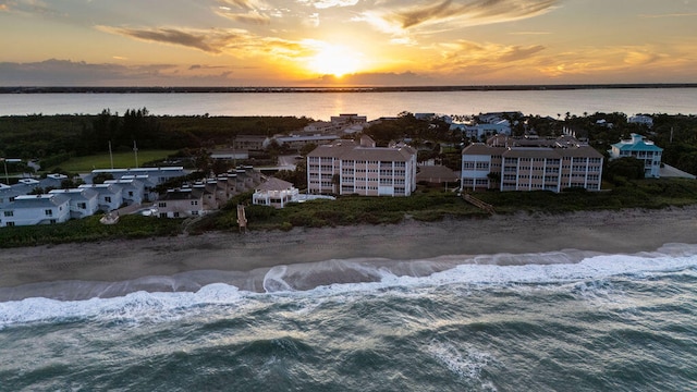 aerial view at dusk featuring a view of the beach and a water view