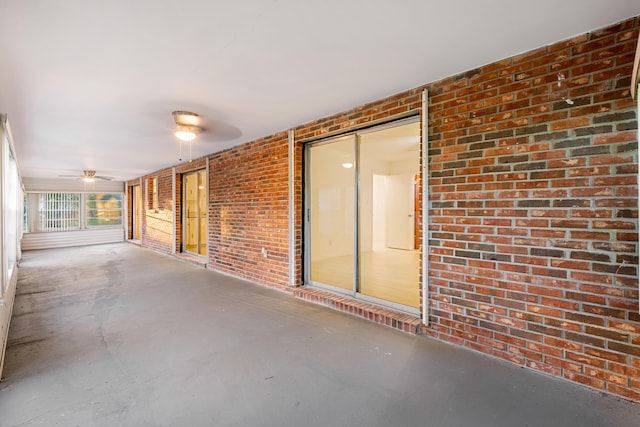 interior space featuring ceiling fan, brick wall, and concrete floors