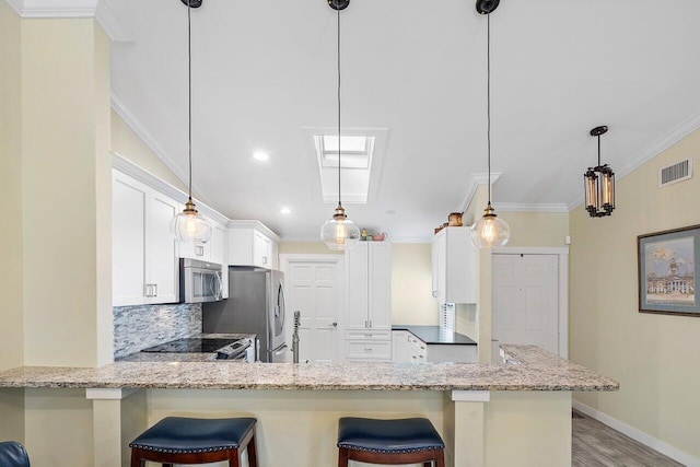 kitchen with stainless steel appliances, kitchen peninsula, a kitchen bar, decorative backsplash, and white cabinets