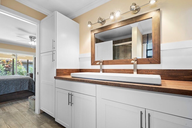 bathroom with ceiling fan, wood-type flooring, vanity, a shower with shower door, and ornamental molding